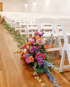 the aisle is lined with white chairs and colorful flowers