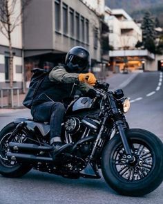 a man riding on the back of a black motorcycle down a street next to tall buildings