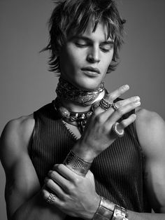 a young man with his hands on his chest wearing bracelets and rings, posing for a black and white photo