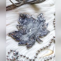 a silver leaf brooch sitting on top of a white fur covered floor next to beads