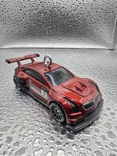 a red toy car sitting on top of a silver table covered in water drops and raindrops