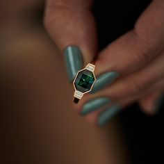 a woman's hand holding a ring with a green stone on it and some nails