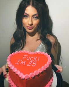 a woman holding a heart shaped cake with the words f i m 25 written on it