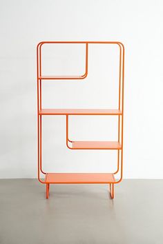 an orange shelf sitting on top of a cement floor next to a white wall,