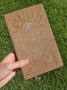 a hand holding up a brown book with writing on it