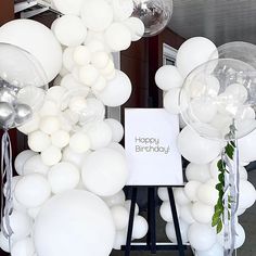 white balloons are arranged in the shape of an arch with a sign that says happy birthday