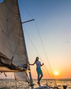 a woman standing on the deck of a sailboat at sunset