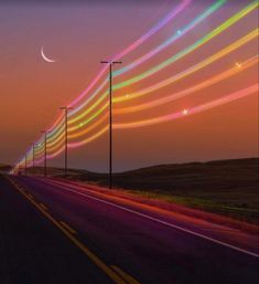 a long line of street lights on the side of a road at night with colorful streaks in the sky