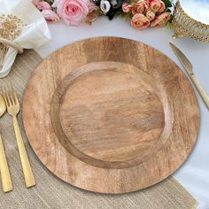 an empty wooden plate on a table with goldware and flowers in the back ground