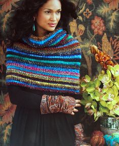 a woman wearing a multicolored knitted shawl next to a potted plant