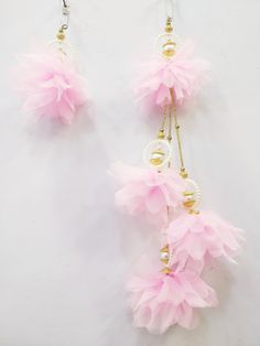 three pink feathers hanging from hooks on a white wall next to pearls and gold beads