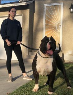 a woman standing next to a brown and white dog on a leash in front of a house