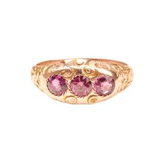 An incredible Victorian Etruscan 12K pink sapphire three-stone band ring. Features engraved floral and scroll motifs with three round-cut pink sapphires. The stones sit flush in round jagged settings and really pop against the gold band.  This ring has not been appraised but the stones are believed to be natural and remain in great condition with minimal surface wear. The gold facade has a polished finish with only minor tarnishing. There are no notable hallmarks or makers mark but the gold has Elegant Three Stone Pink Sapphire Jewelry, Elegant Pink Ruby Three Stone Ring, Pink Three Stone Ruby Ring, Elegant Pink Three-stone Ruby Ring, Pink Heirloom Birthstone Jewelry, Pink Hallmarked Victorian Ruby Ring, Victorian Pink Hallmarked Ruby Ring, Pink Victorian Hallmarked Ruby Ring, Victorian Style Pink Round Rings