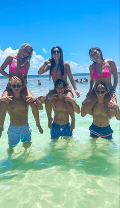 a group of people standing in the ocean with one man on his shoulders and two women on their backs