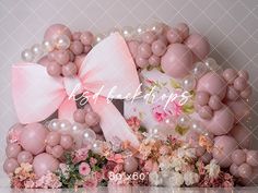 pink and white balloons are arranged in the shape of a bow with flowers around it