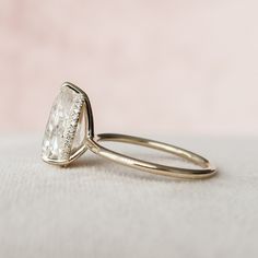 an engagement ring with a pear shaped diamond in the center on a white cloth background