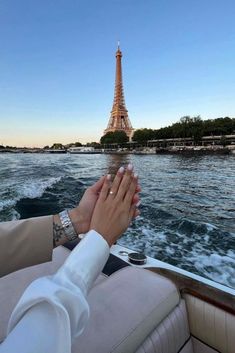 two people holding hands while on a boat in front of the eiffel tower