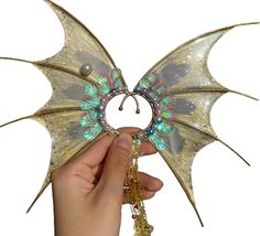 a hand holding a dragon shaped brooch with green and blue beads on it's wings