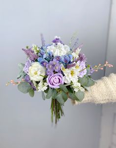 a woman holding a bouquet of flowers in her hand with purple, white and blue colors