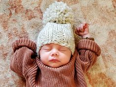 a baby is wearing a knitted hat and laying on its back with it's hands behind his head