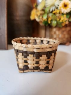 a woven basket sitting on top of a white table next to a vase with flowers in it