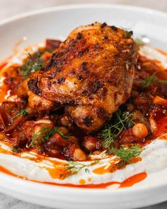 a close up of a plate of food with meat and beans on it, garnished with herbs