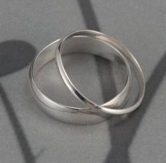 two silver wedding rings casting a shadow on the ground with long shadows behind them, in front of a gray background