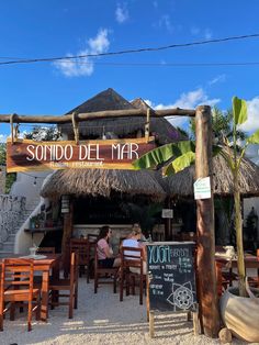 people sitting at tables in front of a restaurant with tiki huts on the roof