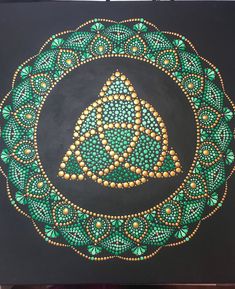 a painting with green and gold designs on black paper, in the shape of a circle