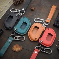 four different colored leather keychains are laying on a table with pine cones and other items