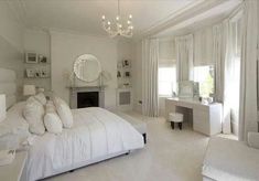 a bedroom with white furniture and chandelier hanging from the ceiling in front of a fireplace