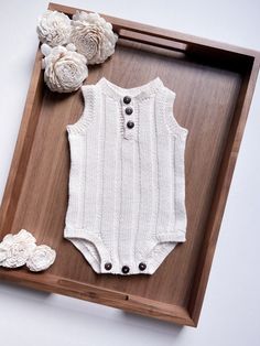 a baby's bodysuit and shoes are on display in a wooden box next to flowers