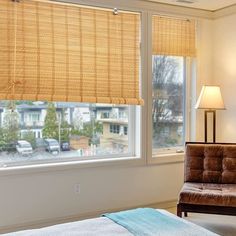 a bedroom with a bed, chair and window covered in bamboo blind shades on the windowsill