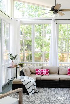 a living room filled with lots of furniture next to a large glass window covered in white curtains