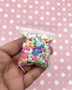 a hand holding a bag filled with lots of sprinkles on top of a pink background