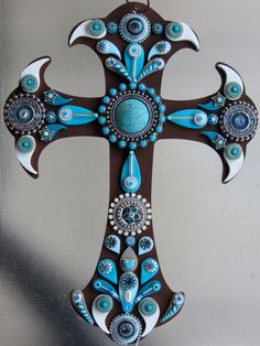 a decorative cross with blue and white designs on it's sides, hanging from a wall