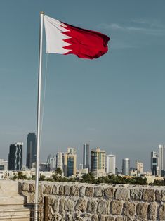 a red and white flag flying in front of a cityscape