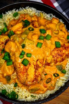 a skillet filled with rice and chicken covered in sauce on top of a wooden table