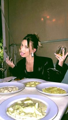 a woman sitting at a table with plates of food and wine in front of her