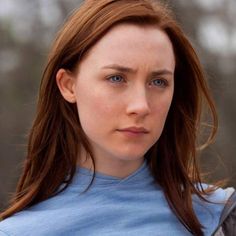 a close up of a person wearing a blue shirt with trees in the back ground