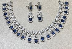 Sapphire Diamond Necklace Set features a stunning blue stone centerpiece surrounded by sparkling CZ American diamonds. The set includes a matching ring, making it a perfect statement piece for a contemporary Indian bride. Ideal as a wedding gift, it exudes elegance and modern sophistication. *𝐏𝐑𝐎𝐃𝐔𝐂𝐓 𝐃𝐄𝐓𝐀𝐈𝐋* * 𝐌𝐚𝐭𝐞𝐫𝐢𝐚𝐥: Brass * 𝐏𝐥𝐚𝐭𝐢𝐧𝐠: White Rhodium Plated * 𝐒𝐭𝐨𝐧𝐞: AAA-quality CZ Diamond & Sapphire. *𝐃𝐈𝐌𝐄𝐍𝐒𝐈𝐎𝐍𝐒* *𝐍𝐞𝐜𝐤𝐥𝐚𝐜𝐞* * 𝐖𝐞𝐢𝐠𝐡𝐭: 56 gm Fine Jewelry With Blue Stones, Blue Fine Jewelry With Stones, Blue Stones Fine Jewelry, Fine Blue Jewelry With Stones, Blue Crystal Jewelry Sets For Wedding, Wedding Jewelry With Sapphire And Diamond Accents, Dazzling Sapphire Jewelry For Wedding, Dazzling Sapphire Wedding Jewelry, Elegant Blue Bridal Sets Gift