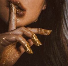 a woman with gold glitters on her face and hand holding up to her mouth