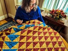 a woman sitting in front of a quilt on top of a wooden table next to a window