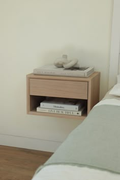 a nightstand with two books on it next to a bed