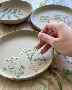 someone is painting flowers on plates with white paint and green stems in the center, while another person holds their hand out to touch them