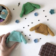 crocheted sweaters and mittens laid out on a table with chocolate bar