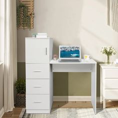 a white desk with a laptop on top of it next to a plant and window