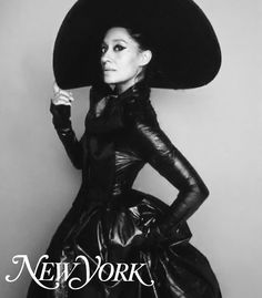 a woman in a black dress and large hat posing for a magazine cover with her hands on her hips