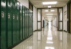 an empty hallway with green lockers on both sides and white flooring in the middle