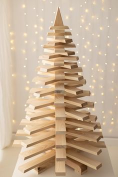 a wooden christmas tree made out of wood planks on a white surface with lights in the background